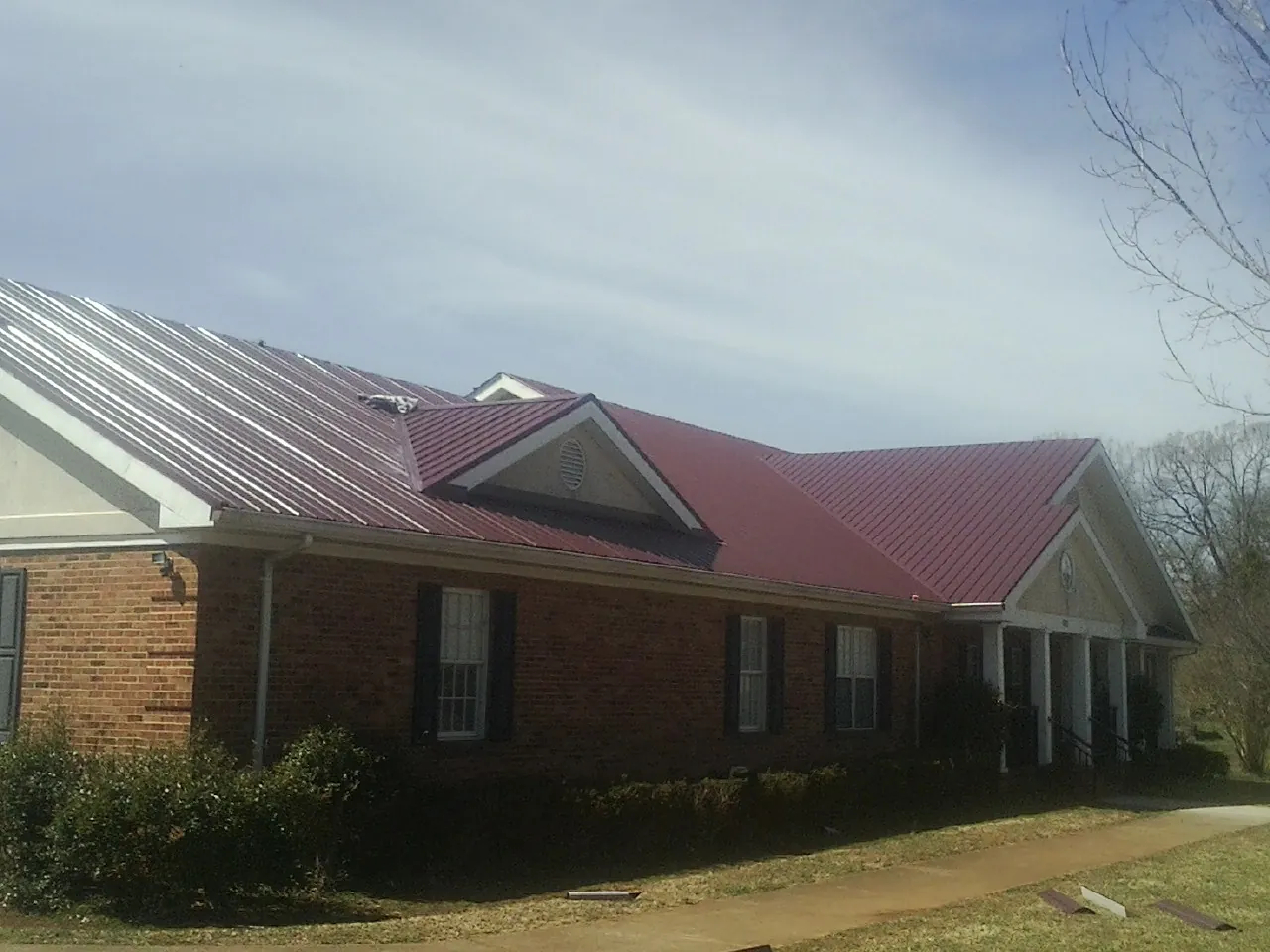 Red metal roof with gabled entries on a long brick building, from a Hail Damage Roof Repair job in Effingham